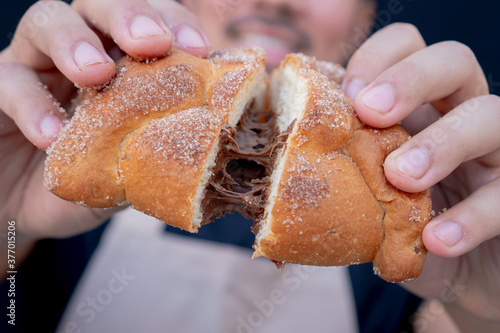 Delicious traditional Mexican pan de muerto or bread or dead stuffed with chocolate, broken in half by two hands.