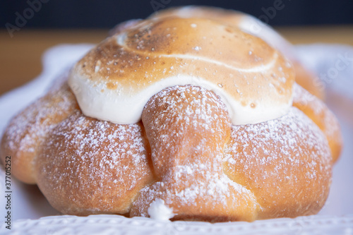 Exquisite pan de muerto or bread of dead adorned with icing on top on a white plate.