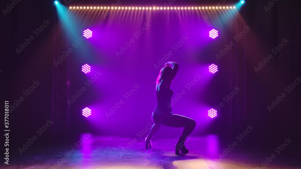 Young hot female dancer erotically moves her body and ass in the rays of purple lights. Silhouette of a woman in heels dancing twerk. Slow motion. Young hot female dancer erotically moves her body and ass in the rays of purple lights. Silhouette of a woman in heels dancing twerk. Slow motion.