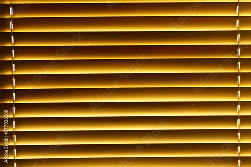 Abstract background - wooden blinds on the window, large brown-golden horizontal stripes lit by the sun