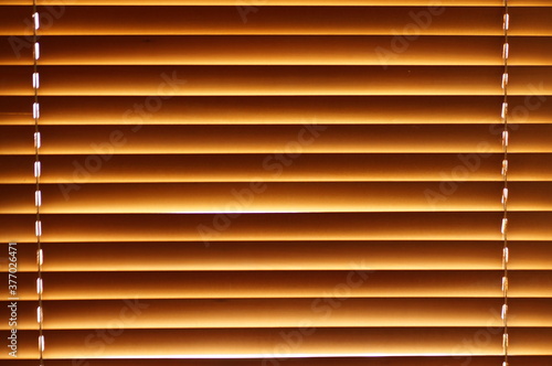 Abstract background - wooden blinds on the window, large brown-golden horizontal stripes lit by the sun