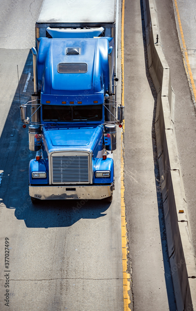 Classic blue big rig semi truck transporting cargo in refrigerated semi trailer with refrigerator unit on the front wall running on the highway road Classic blue big rig semi truck transporting cargo in refrigerated semi trailer with refrigerator unit on the front wall running on the highway road
