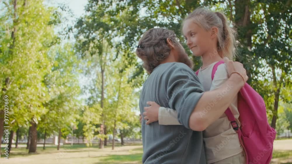 Medium shot of bearded father smiling and hugging cute schoolgirl with backpack, then waving her goodbye Medium shot of bearded father smiling and hugging cute schoolgirl with backpack, then waving her goodbye