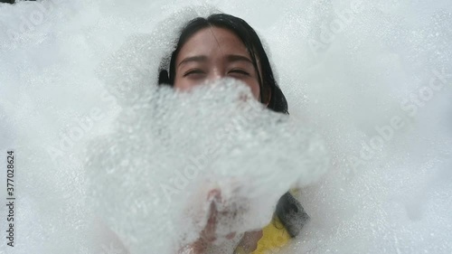smiling and laughing young Asian women covered in soap foam dancing on the party at bright sunny day.