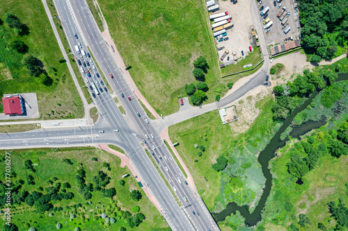 aerial top view of crossroads, roads with car traffic and parking lot with trucks in suburb area