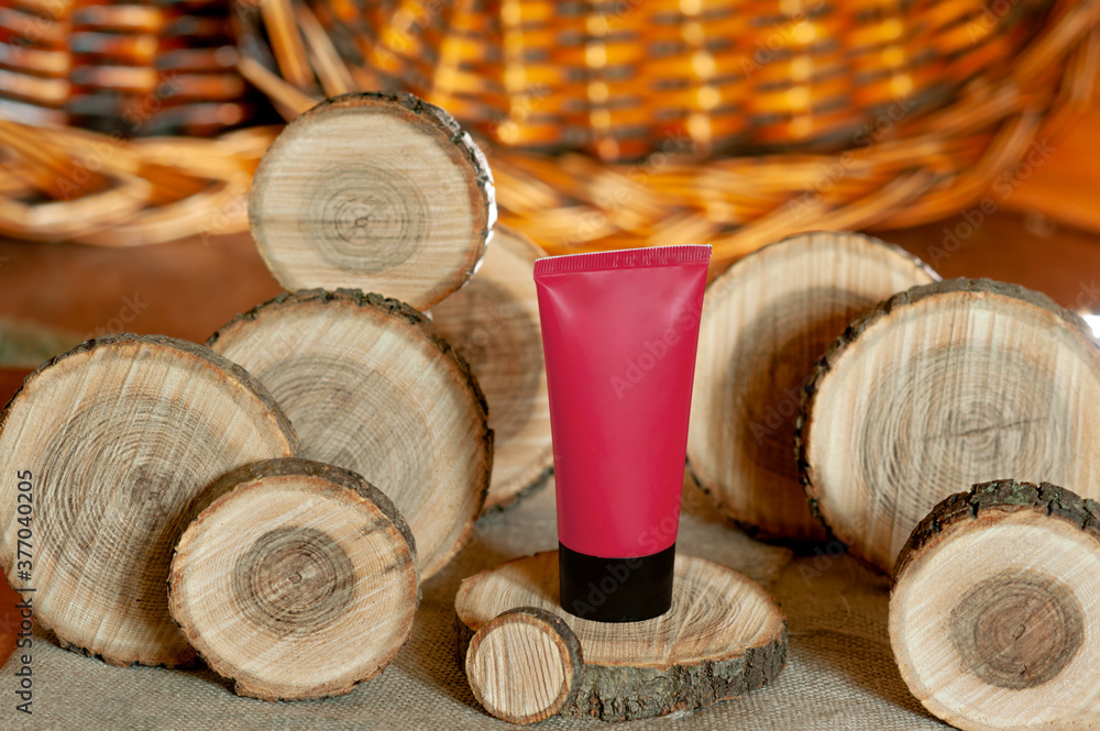 red cosmetic cream tube surrounded by wooden round pieces of different sizes, trendy cosmetic layout