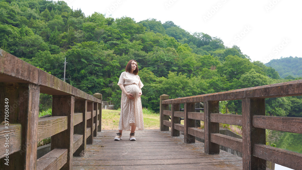 橋の上に立って景色を見ている妊婦さん