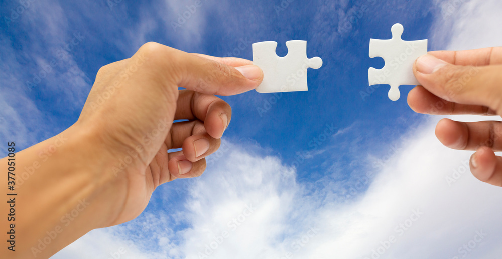 Abstract teamwork and partnership concept with hands holding jigsaws puzzle and blue sky background