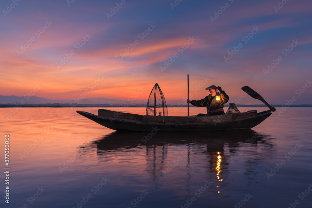 Silhouette of asian fisherman on wooden boat in nature river in the early morning before sunrise