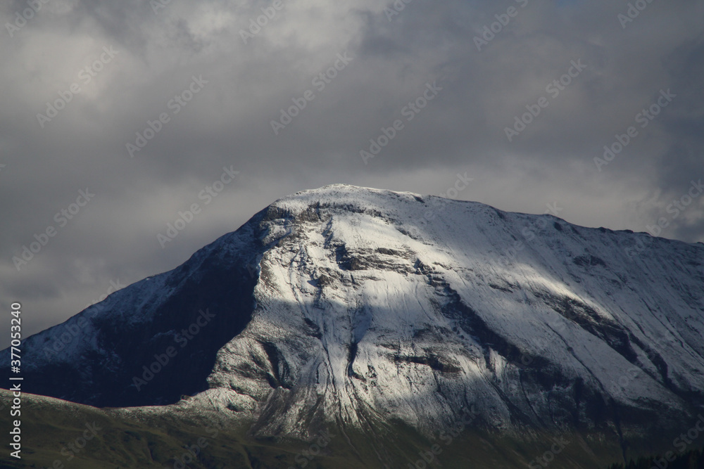 Sonne nach dem Regen auf Schneebedecktem Berg, Wolken im Hintergrund, hoher Kontrast