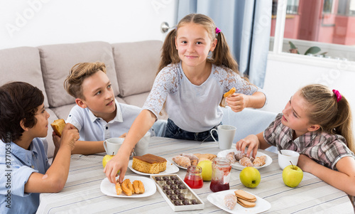 Teenagers friends eating sweet food with tea at the table on sofa