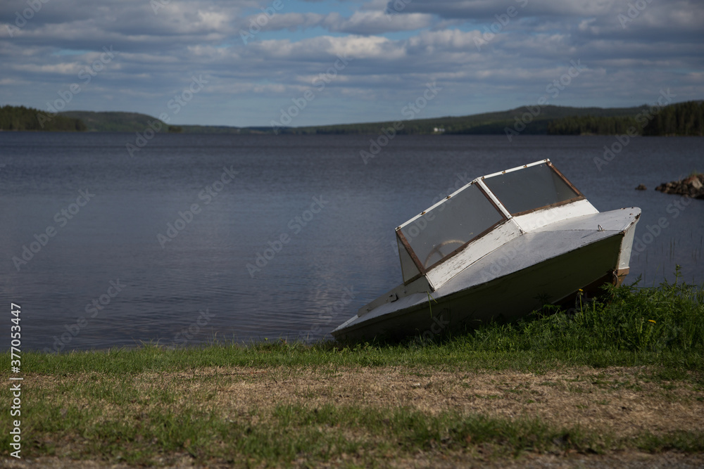Boot am Ufer auf Gras gestrandet, See unter blauem Himmel, Hügel im Hintergrund Boot am Ufer auf Gras gestrandet, See unter blauem Himmel, Hügel im Hintergrund