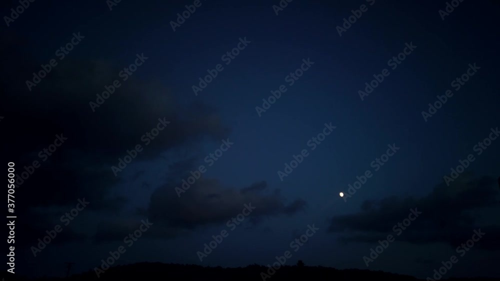 Time lapse: dark grey cumulus and stratus puffs of clouds flow, roll and move towards white full moon in blue evening sky above silhouette hilltop, low angle, day to night Time lapse: dark grey cumulus and stratus puffs of clouds flow, roll and move towards white full moon in blue evening sky above silhouette hilltop, low angle, day to night