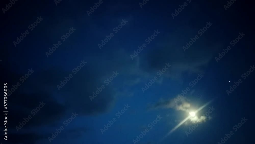 Time lapse: epic shiny flare, glare, beam and ray of full moon in dark crisp blue sky night with grey ominous, eerie and spooky cumulus and stratus puffy clouds flow, roll and move in atmosphere Time lapse: epic shiny flare, glare, beam and ray of full moon in dark crisp blue sky night with grey ominous, eerie and spooky cumulus and stratus puffy clouds flow, roll and move in atmosphere