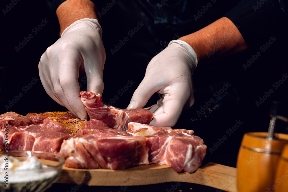 A man in gloves prepares and marinates pork with spices for cooking kebabs, uses salt, curry and basil.