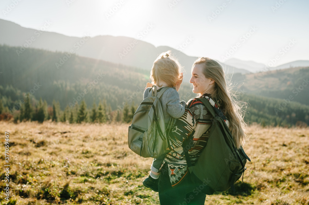 Mom with backpack and child walk in autumn grass. The daughter and mother walking on nature. Family spending time together in mountain on vacation. Holiday trip concept. World Tourism Day. Back view. Mom with backpack and child walk in autumn grass. The daughter and mother walking on nature. Family spending time together in mountain on vacation. Holiday trip concept. World Tourism Day. Back view.