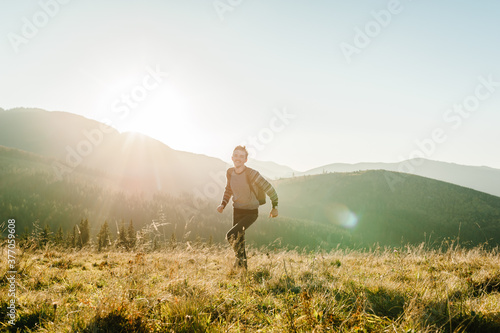 Happy traveler with a backpack running and walking on the mountain at sunset. Man enjoying the view of nature. Tourist travel concept. Hiker in country Europa. World Tourism Day.