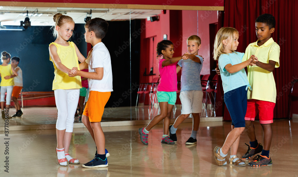 Group of glad positive smiling childrens trying dancing with partner in classroom