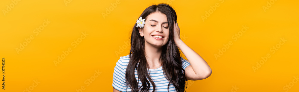 brunette young woman with flowers in hair and closed eyes smiling isolated on yellow, panoramic shot - obrazy, fototapety, plakaty 