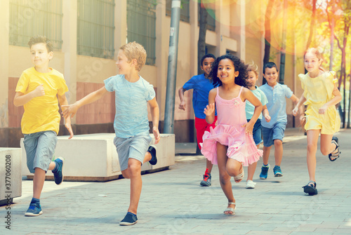 Group of joyful children running down the summer city street