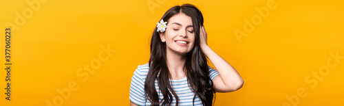 brunette young woman with flowers in hair and closed eyes smiling isolated on yellow, panoramic shot
