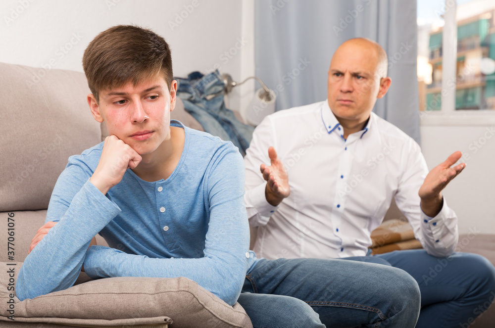 Portrait of son ignoring irritated father sitting in home interior