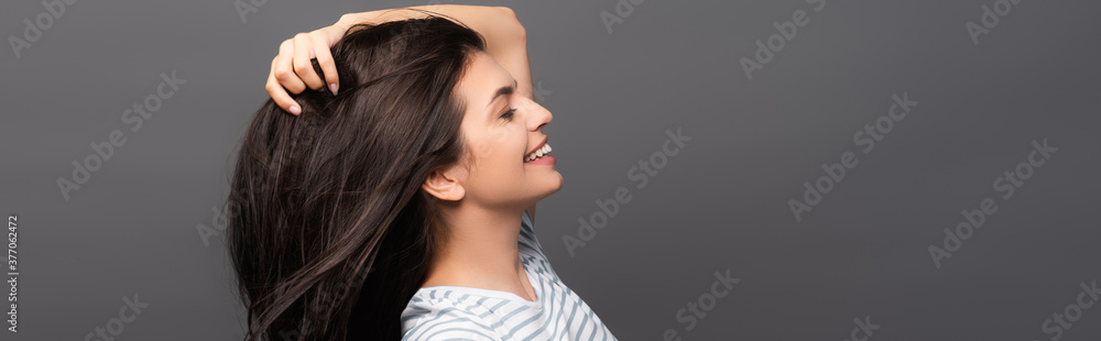 side view of brunette woman with closed eyes smiling and touching hair isolated on black, panoramic shot side view of brunette woman with closed eyes smiling and touching hair isolated on black, panoramic shot