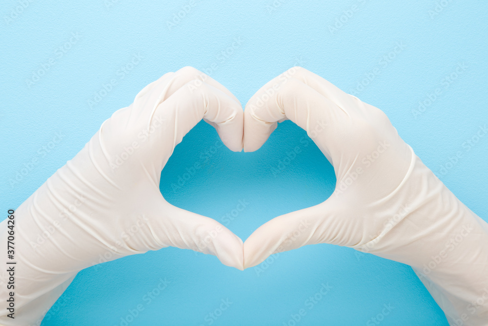 Doctor hands in white rubber protective gloves showing heart shape on blue table background. Pastel color. Closeup. Point of view shot. Healthcare concept. Top down view. Doctor hands in white rubber protective gloves showing heart shape on blue table background. Pastel color. Closeup. Point of view shot. Healthcare concept. Top down view.
