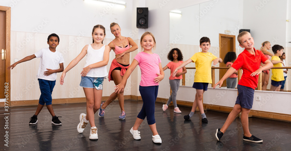 Fototapeta premium Group of tweens doing dance workout with female coach in classic choreography class..
