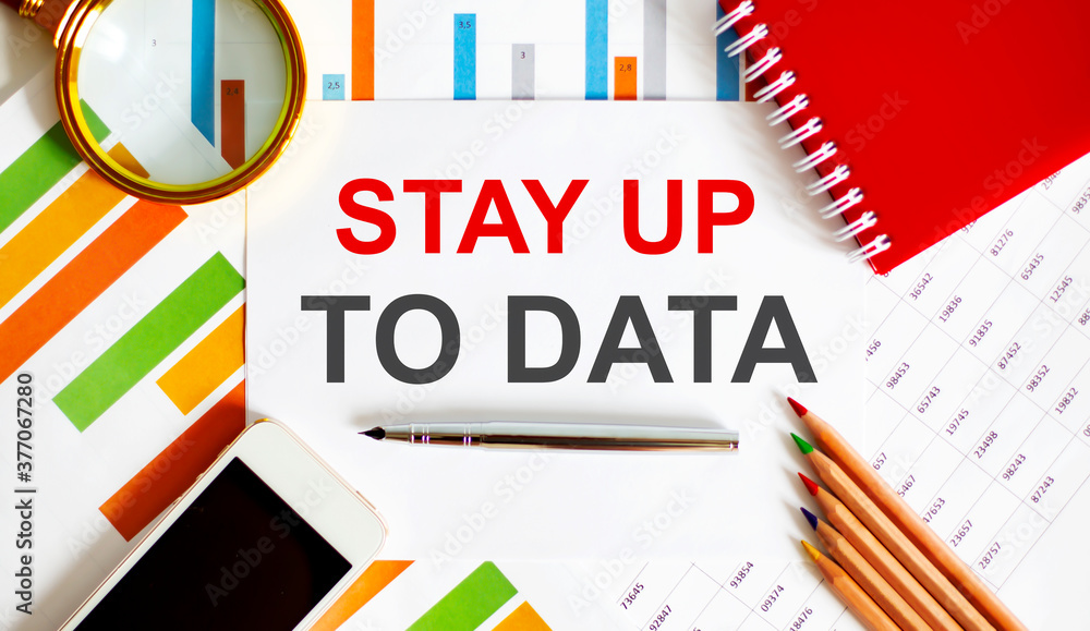 Text STAY UP TO DATA on the notepad with office tools, pen on financial report