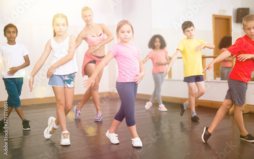 Cheerful preteen girls and boys hip hop dancers doing dance workout with female trainer during group class