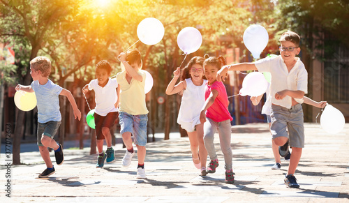 Group of happy kids with balloons running in race in the street and laughing outdoors