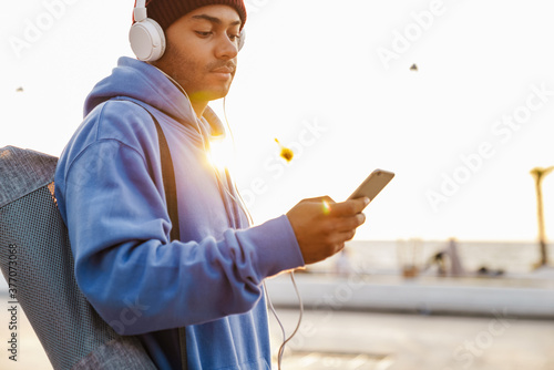 Image of african american sportsman using cellphone and headphones