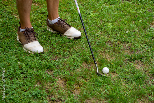 View of man's feet with golf shoes with iron and cue ball, ready to hit, on green grass, horizontal