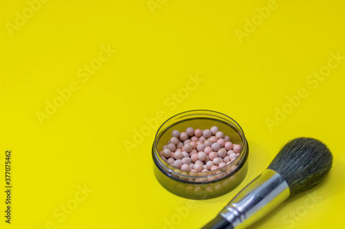 Cosmetics on yellow background and place for an inscription. Ball blush and makeup brush close-up, shallow depth of field, copy space