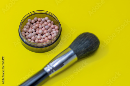 Cosmetic powder balls blush and makeup brush close-up, shallow depth of field. Bright yellow background. Brush is out of focus