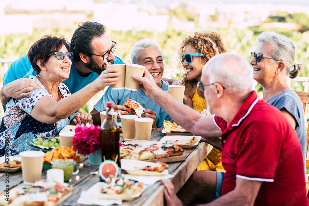 Group of different ages people celebrate and eat together in friendship outdoor at home - happy young, adult and senior have fun clinking and enjoying food on a wooden table - celebration Group of different ages people celebrate and eat together in friendship outdoor at home - happy young, adult and senior have fun clinking and enjoying food on a wooden table - celebration