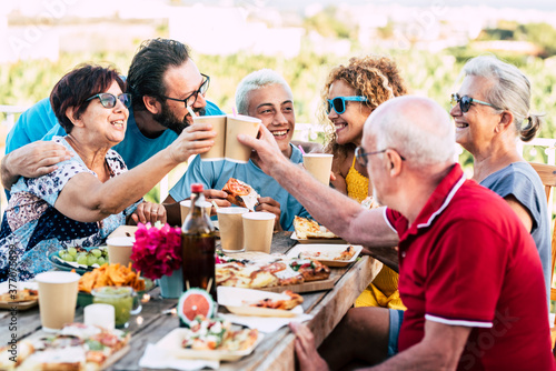 Group of different ages people celebrate and eat together in friendship outdoor at home - happy young  adult and senior have fun clinking and enjoying food on a wooden table - celebration 