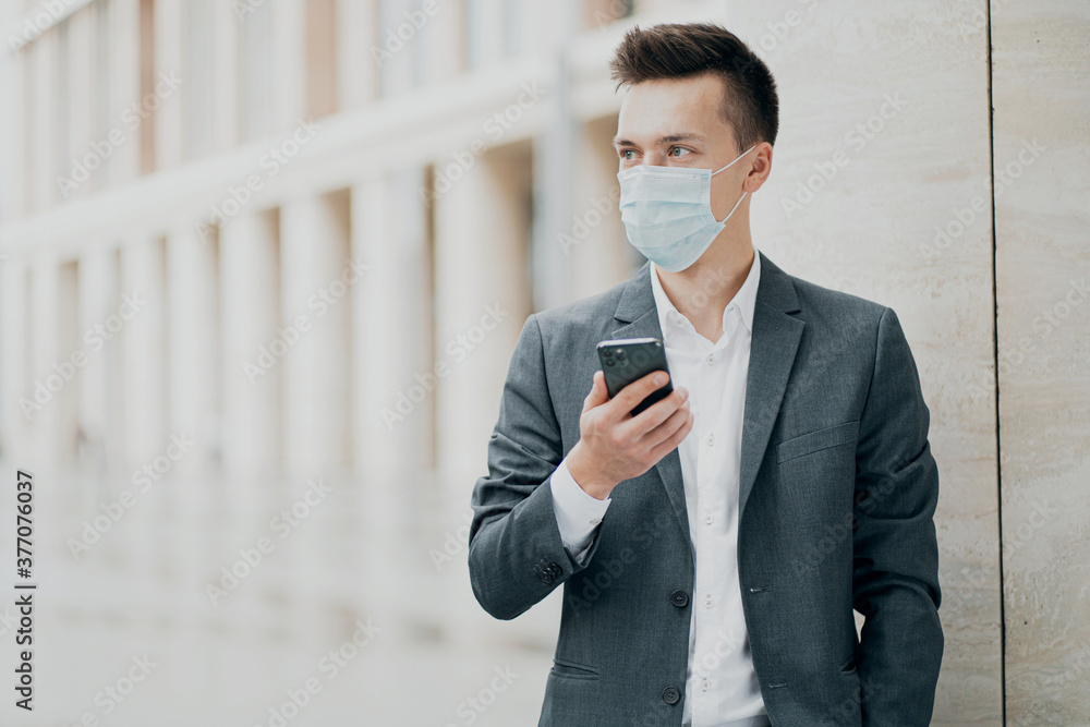 face blue protective mask pandemic coronavirus 19. portrait of a serious smart man student holding a new phone writes a message to a partner. Grey business suit, dark hair face blue protective mask pandemic coronavirus 19. portrait of a serious smart man student holding a new phone writes a message to a partner. Grey business suit, dark hair