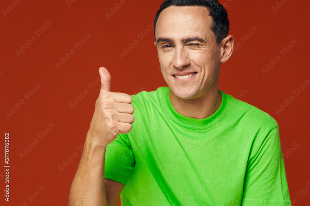 A man in a green T-shirt on a red background winks at the camera A man in a green T-shirt on a red background winks at the camera