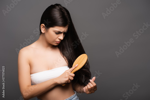 worried brunette woman brushing hair isolated on black