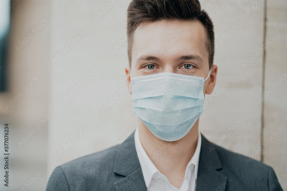 blue protective mask from the coronavirus 19 pandemic on the face. portrait of a man businessman holding a new phone calls a partner wants to talk about work. gray suit. a good day blue protective mask from the coronavirus 19 pandemic on the face. portrait of a man businessman holding a new phone calls a partner wants to talk about work. gray suit. a good day