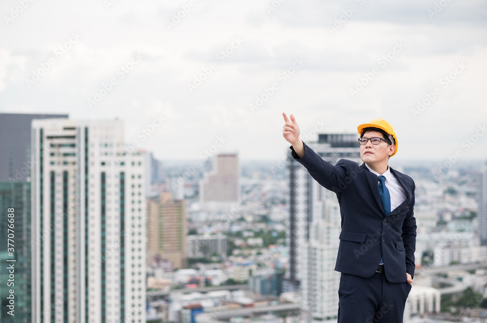 Young handsome asian civil engineer standing wearing helmet yellow hard hat in business suite on building urban cities background. Young handsome asian civil engineer standing wearing helmet yellow hard hat in business suite on building urban cities background.