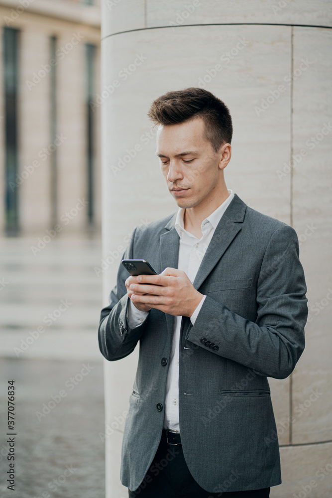 a male student holding a new phone is texting with a friend. Grey business suit, brunette hair stylish barbershop hair salon. a male student holding a new phone is texting with a friend. Grey business suit, brunette hair stylish barbershop hair salon.