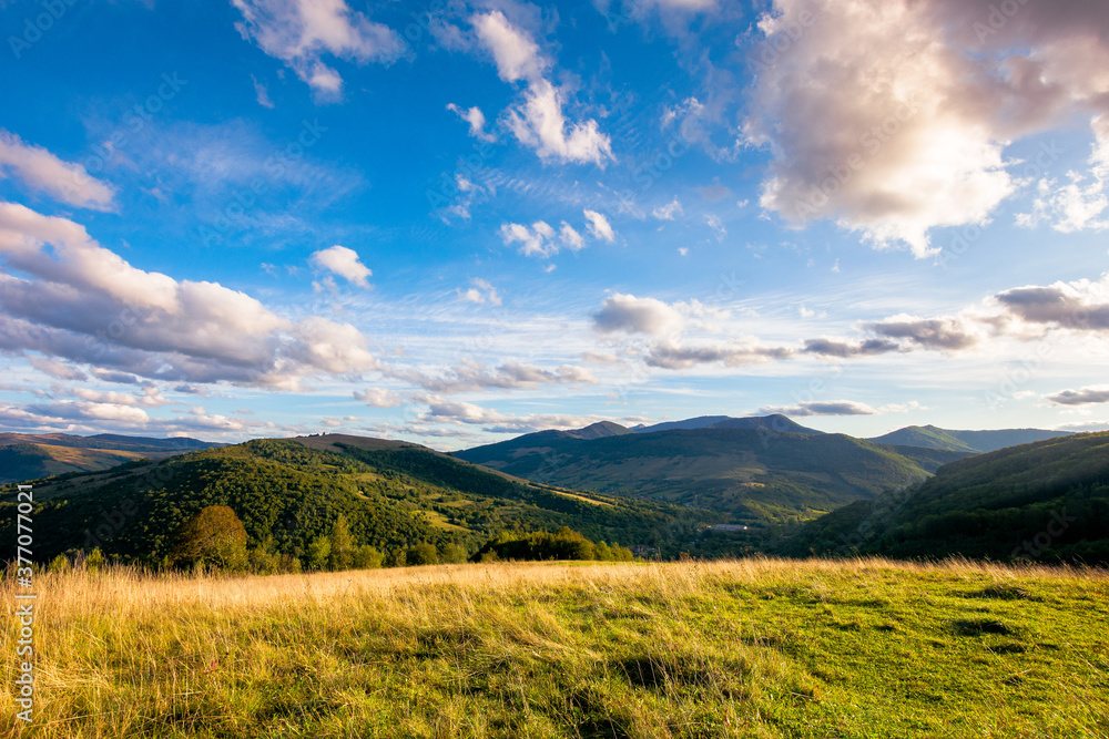 rural landscape in mountains at sunset. grassy pasture on the hill in evening light. high mountains in the distance. beautiful clouds on the blue sky. wonderful early autumn scenery