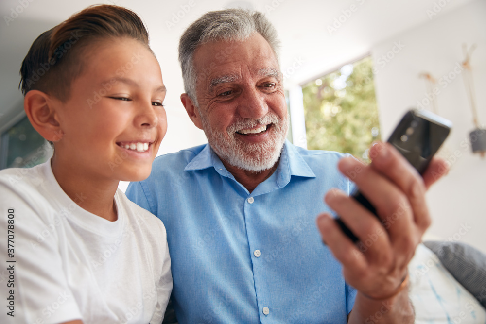 Hispanic Grandson Showing Grandfather How To Use Mobile Phone At Home Hispanic Grandson Showing Grandfather How To Use Mobile Phone At Home