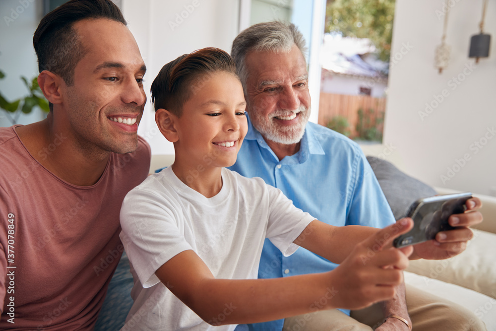 Multi-Generation Male Hispanic Family On Sofa At Home Posing For Selfie On Mobile Phone Multi-Generation Male Hispanic Family On Sofa At Home Posing For Selfie On Mobile Phone