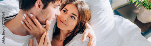 Panoramic shot of young woman touching neck of boyfriend on bed at home