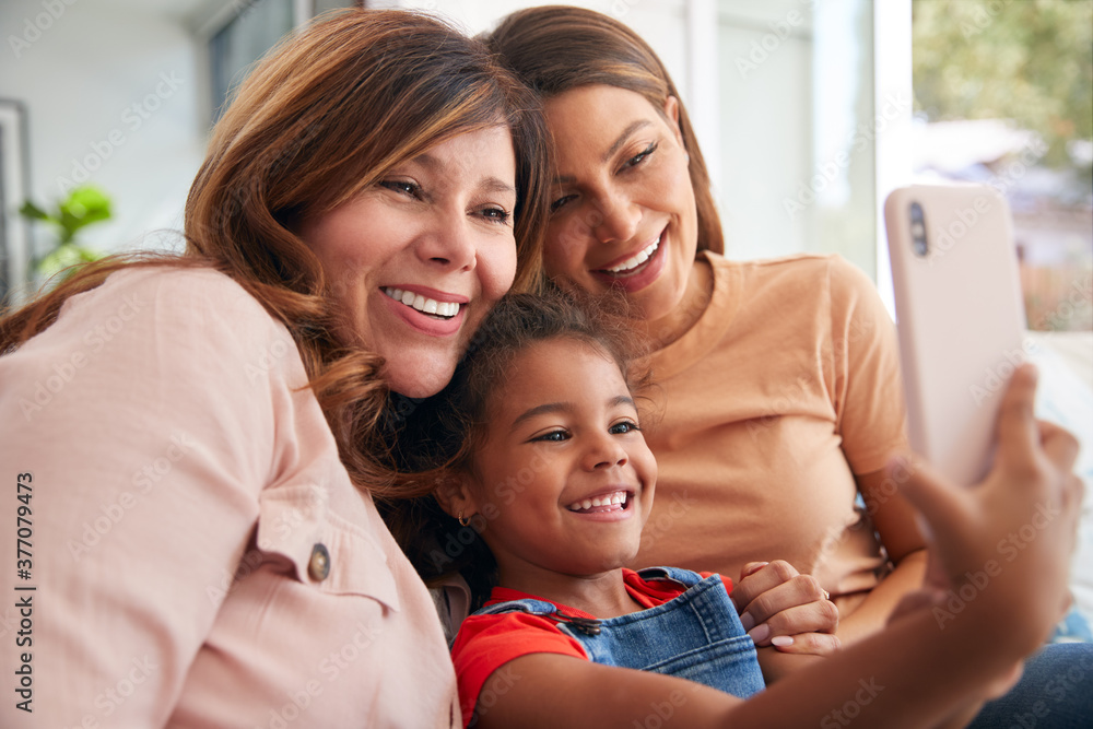 Multi-Generation Female Hispanic Family On Sofa At Home Posing For Selfie On Mobile Phone Multi-Generation Female Hispanic Family On Sofa At Home Posing For Selfie On Mobile Phone