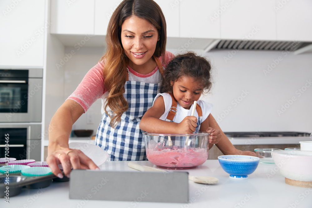 Hispanic Mother And Daughter In Kitchen Following Cake Recipe On Digital Tablet Together Hispanic Mother And Daughter In Kitchen Following Cake Recipe On Digital Tablet Together